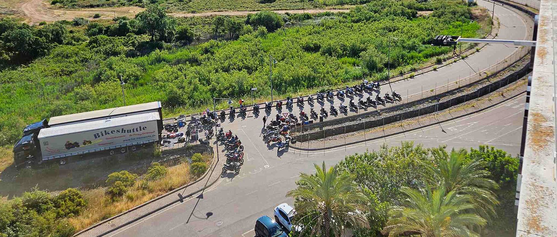Viele Motorräder stehen an einer Straße, zwei LKW mit der Aufschrift "Bikeshuttle" stehen daneben