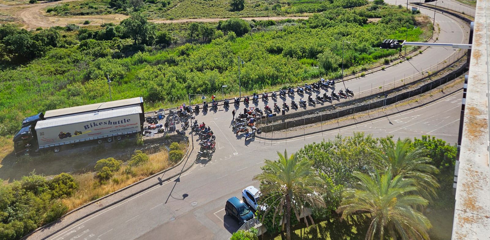 Viele Motorräder stehen an einer Straße, zwei LKW mit der Aufschrift "Bikeshuttle" stehen daneben